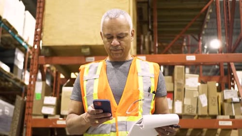 Mature african american warehouse manager reads email on smart phone