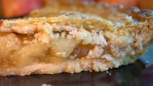 Close up of a flaky apple pie on a dark plate and red and white checker cloth