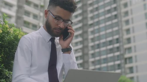 Man Working on Laptop While Talking on Phone