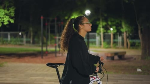 Night Park Contemplation Woman With Bike Under Lamp Quiet Evening Scene With Reflective Woman