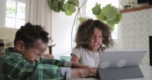 Two Children Using Tablet Indoors at Table