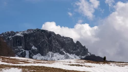 Time Lapse of Dramatic mountain range dominates the scene partially covered in snow under a bright s