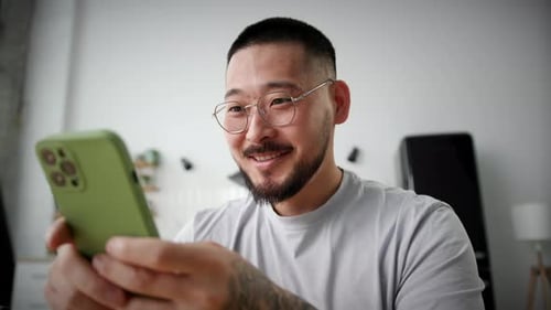 Smiling Man Uses Smartphone Indoors