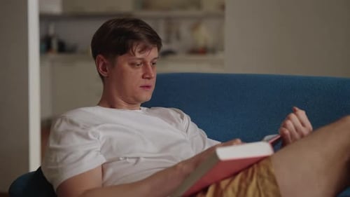 Young Adult Reading a Book on Blue Couch