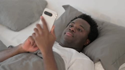 Young Adult Using Phone Lying in Bed