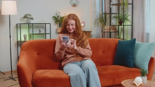 Smiling Woman Using Smartphone on an Orange Couch