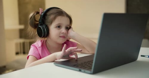 Small Girl Wearing Headphones Studying Online From Home with Distance Teacher