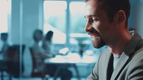 Portrait of a Young Businessman Sitting and Using a Laptop Smiles Looking at the Laptop Business