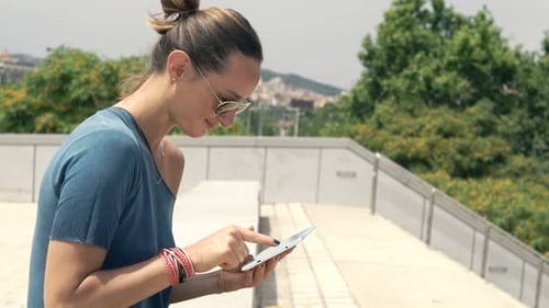 Young Woman Browsing Internet on Tablet Sitting on Bench in City 30s