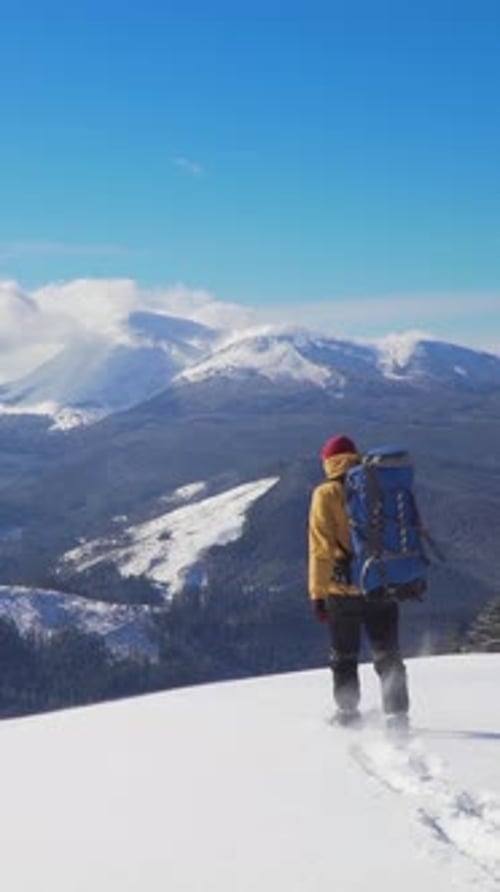 Hiker Celebrates at the Summit During Winter Hike in Snowy Mountain Landscape Under Clear Skies