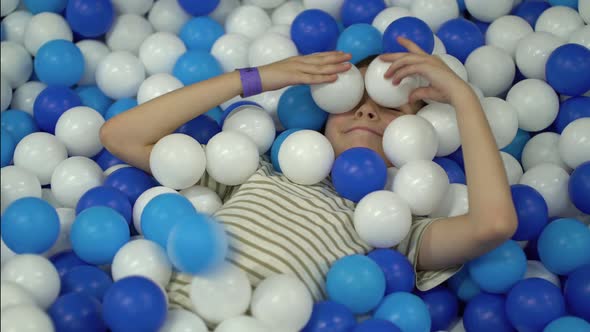 The Boy Fools Around in the Pool with Colorful Plastic Balls and Throws ...