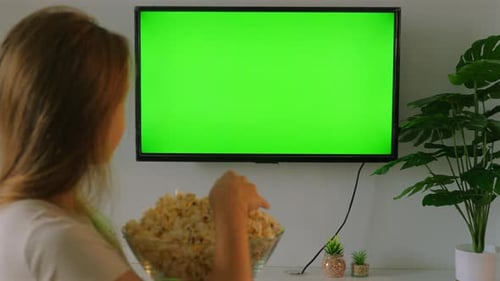 Woman Eating Popcorn While Watching TV with Green Screen at Home