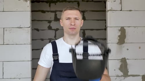Man Puts on Welding Helmet in Construction Site