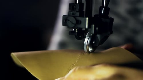 Craftsman hands skillfully stitching leather material with sewing machine in workshop