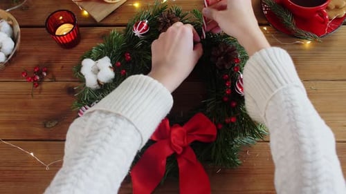 Las manos femeninas crean una corona navideña con adornos de abeto en casa para las vacaciones de invierno