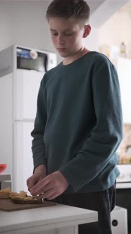 Adolescent préparant le petit-déjeuner en étalant du beurre sur du pain dans la cuisine, atmosphère décontractée