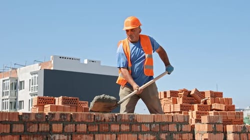 Construction Worker Laying Bricks on Wall Spreading Cement Mortar with Trowel at New Residential