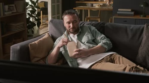 Man Relaxes on Couch and Eats Takeout