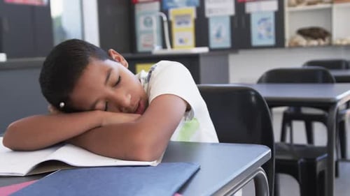 In school, in the classroom, a young student is yawning at his desk with copy space