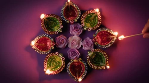 Lighting Diwali Oil Lamps with Flowers on Purple
