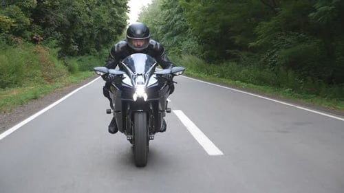 Junger Mann mit Helm fährt auf modernem Sportmotorrad auf ländlicher Waldstraße Motorradfahrer fährt mit seinem