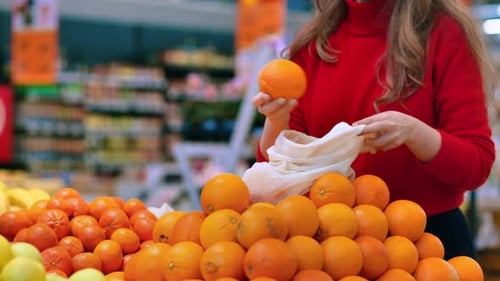 Mujer recogiendo naranjas en una bolsa reutilizable en una tienda. Temáticas del Día de la Tierra y la Ecología