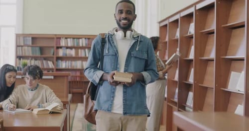 Slow Motion Portrait of Cheerful African American Man Standing in Library in College Holding Books