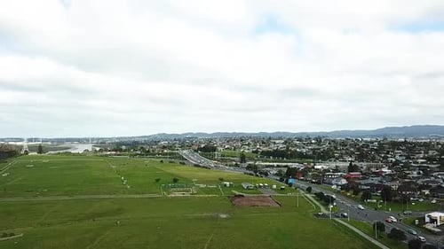 Aerial drone shot flying over a big farm on the left and busy traffic on the right in Auckland, New