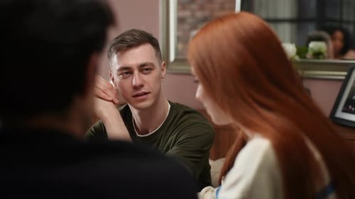Vue latérale rapprochée d'une jeune femme rousse assise autour d'une table avec des amis racontant une histoire