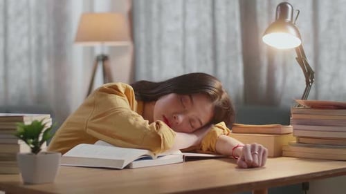 Young Woman Sleeping at Desk Amongst Books