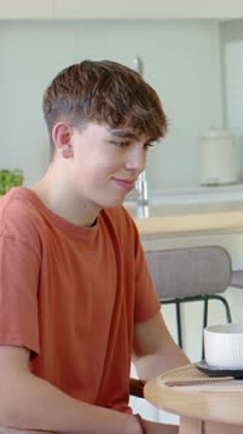 Vertical video: Smiling teen turning to offscreen cue at kitchen, bowl and orange tee, copy space