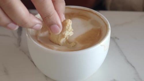 Hand Dips Cookie into Frothy Cup of Coffee