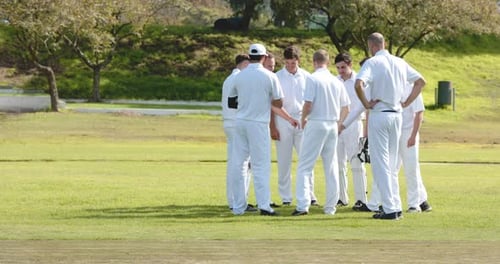 Teams of multiracial male cricket players wearing cricket white on pitch