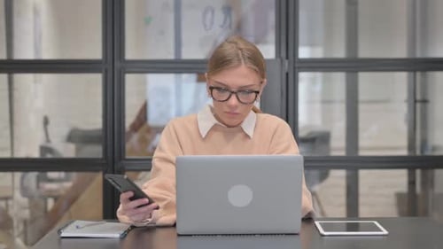 Woman Using Smartphone with Laptop in Office