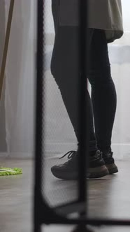 Person Standing Indoors in Casual Outfit and Sneakers Near Window Captured From the Knees Down in
