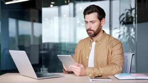 Businessman is using digital tablet sitting at workplace in business office. Handsome bearded
