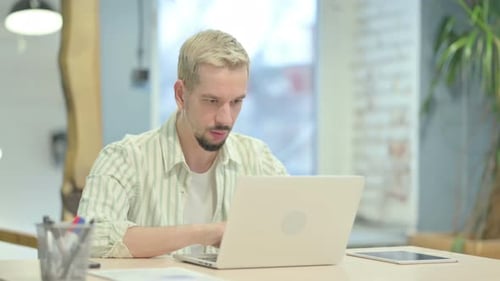 Young Adult Working at Laptop, Looking at Camera