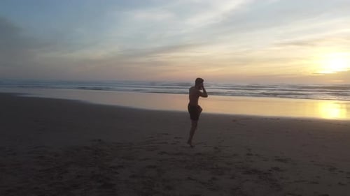 Closer to the subject - Low drone shot panning left, of a man practcing martial arts on a beach in P