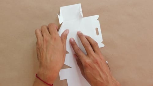 Caja de confitería blanca plegable a mano sobre superficie marrón, vista desde arriba