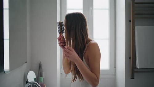 Young Woman Brushing Long Hair in Bright Bathroom