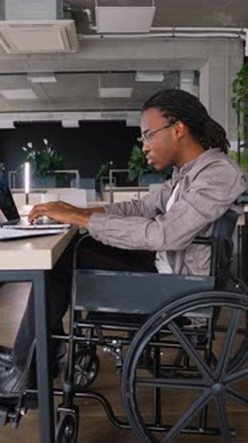 Young Adult in Wheelchair Works on Laptop in Office