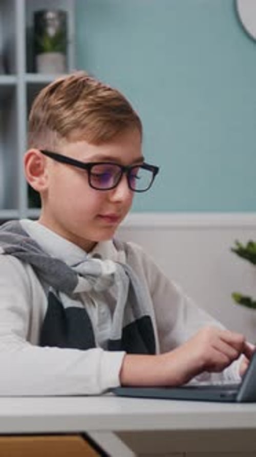 Boy with Glasses Typing on Laptop at Desk Indoors