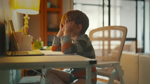 Child Sits at Desk and Watches Computer Screen with Frustration