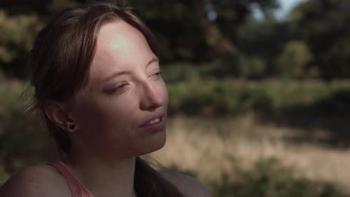 Close up of a woman in a park who is standing in the shadow of a tree with the sun shining on her fa