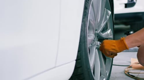 Automechaniker wechselt bei einem Autoservice mit einem Ballonschlüssel ein Rad an einem weißen Luxusauto