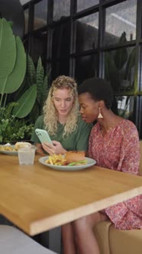 Two Women Looking at Smartphone and Laughing in Cafe