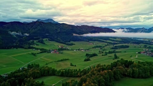 Aerial drone forward moving shot over green farmlands surrounded by mountain range on all sides in N