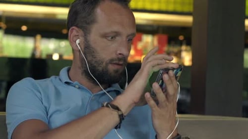 Young Man Watching Movie on Smartphone Sitting on Sofa in Cafe 30s
