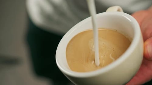 Barista making latte art in a cafe Male hands pouring steam of milk into a cup of Cappuccino