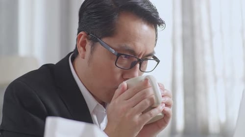 Close Up Of Sick Asian Businessman Drinking Hot Water While Working With Laptop At Home
